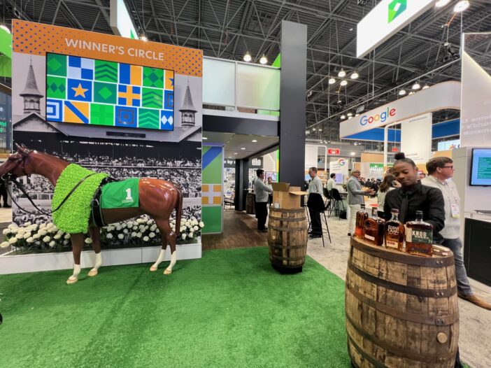 Booth at a trade show with a "Winner's Circle" banner above a horse statue wearing a green blanket.