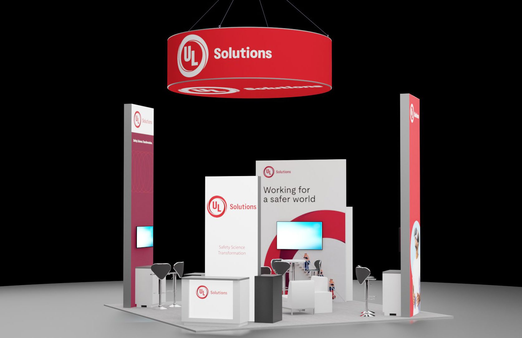 Exhibition booth with red and white UL Solutions branding. It features a table with white chairs, a screen, and industrial light bulb decor, set on a dark carpet.