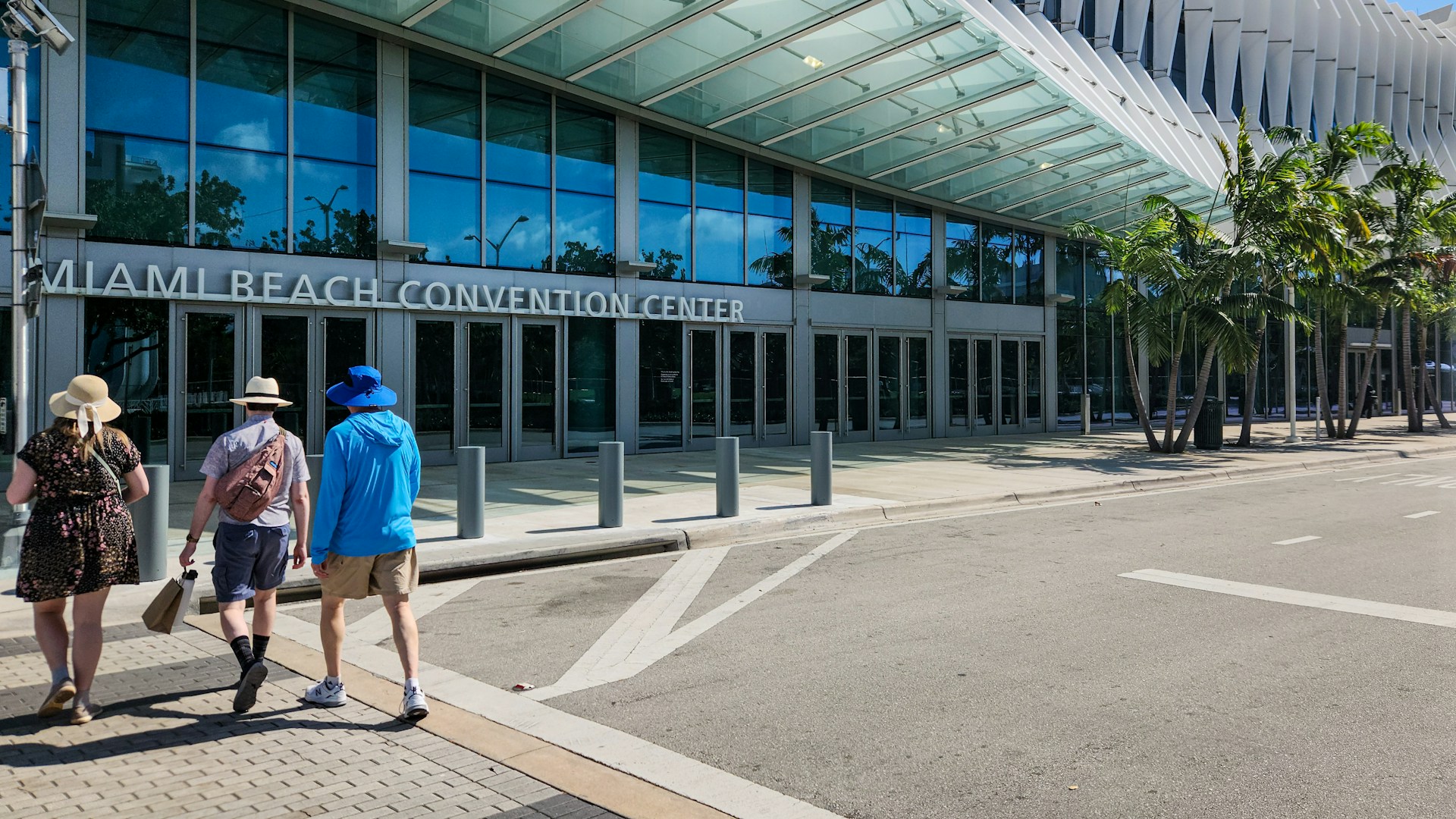 Three people walk towards the Miami Beach Convention Center on a sunny day.
